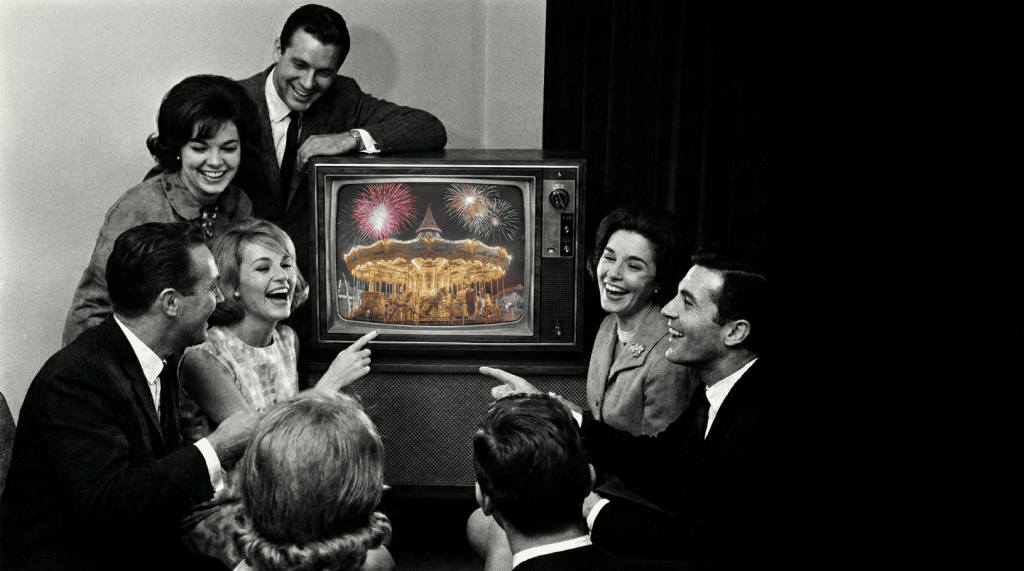 Ett foto på människor i svartvitt med en tv som visar färg-tv i mitten.